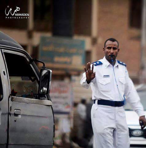 بالصور.. وفي لفتة بارعة.. ضابط بشرطة المرور السودانية يستأذن أسرته وينزل من سيارته لينظم حركة المرور وهو يمازح السائقين (يلا يا حاج حرك عشان تحصل الفطور .. ويا عمو هدئ أدي الخالة دي فرصة عشان تعدي) 3 ضابط_n
